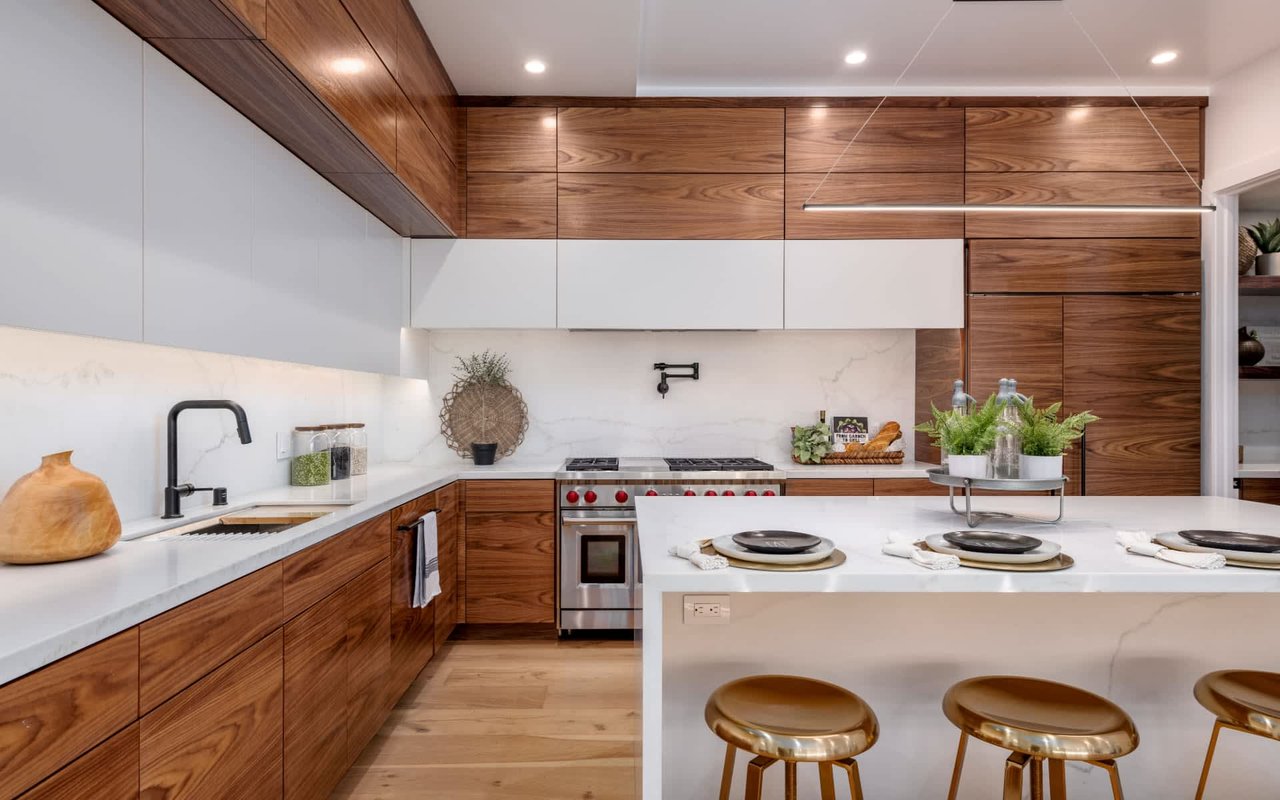 Modern kitchen with walnut cabinetry, marble counters, and a large island with brass stools.
