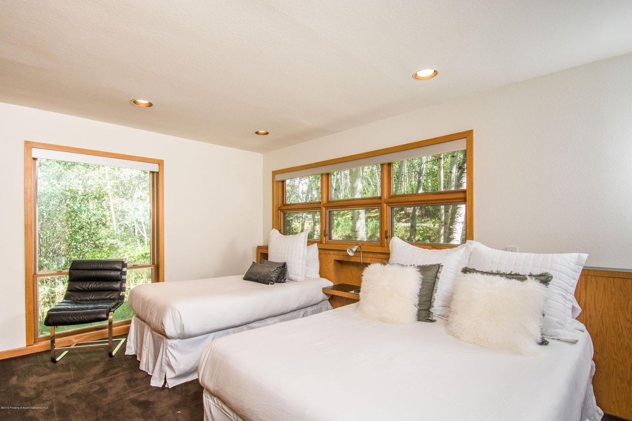 Bedroom with two white beds, wood-trimmed windows, and views of trees.