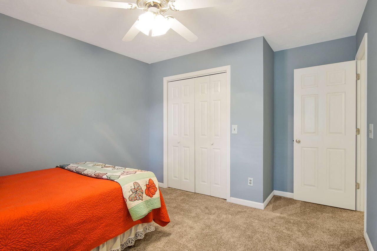 An interior shot of a bedroom with blue walls and a red bedspread. The room has a closet with white doors and carpeted flooring.