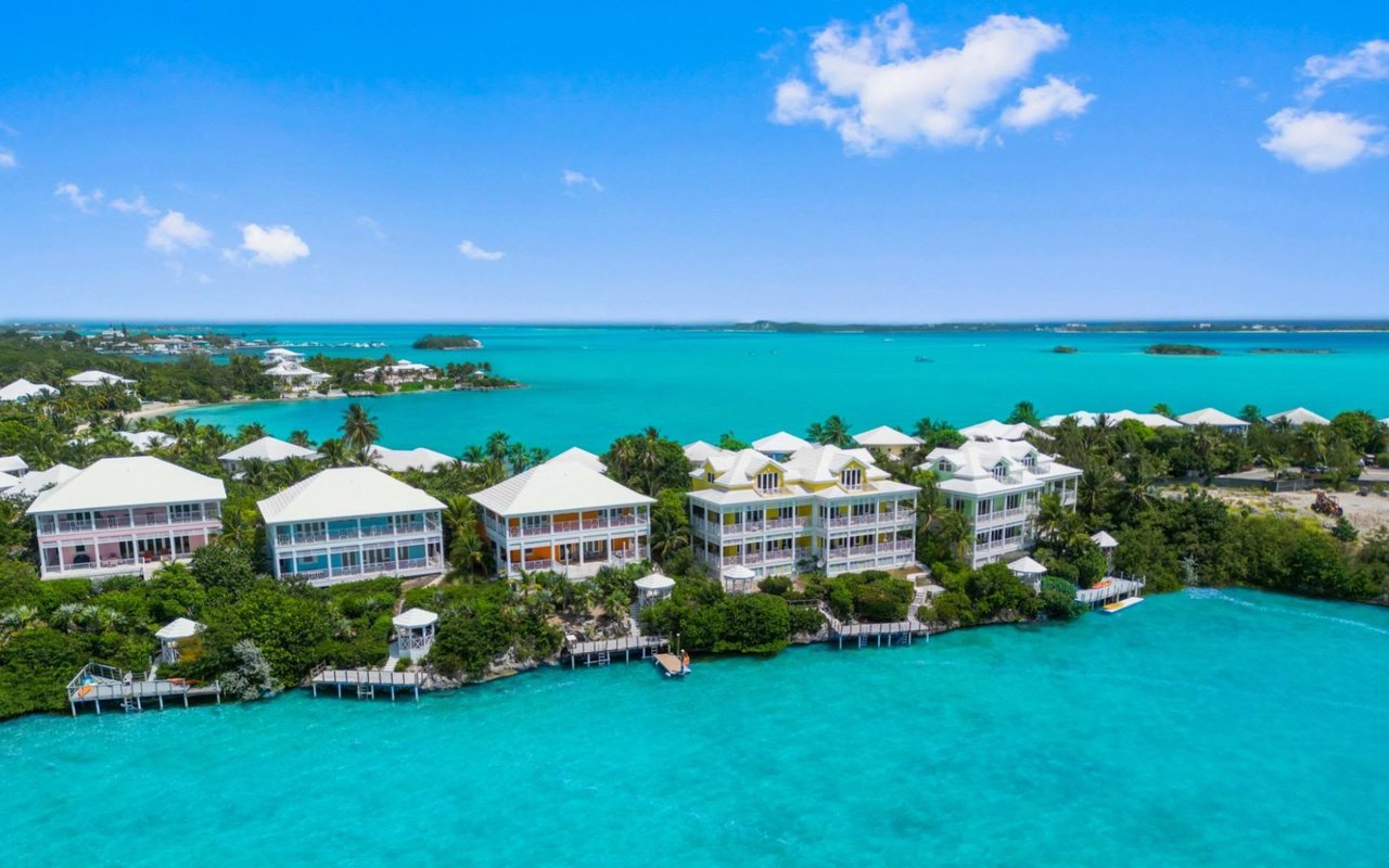 An aerial view of a row of colorful beach houses on the shore of a clear blue ocean.