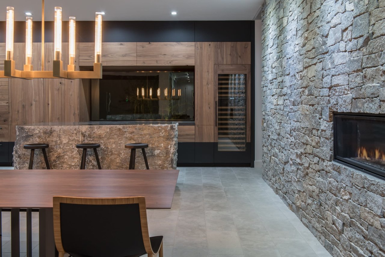 Dining area and bar with a stone fireplace wall, wood cabinetry, and a modern chandelier.