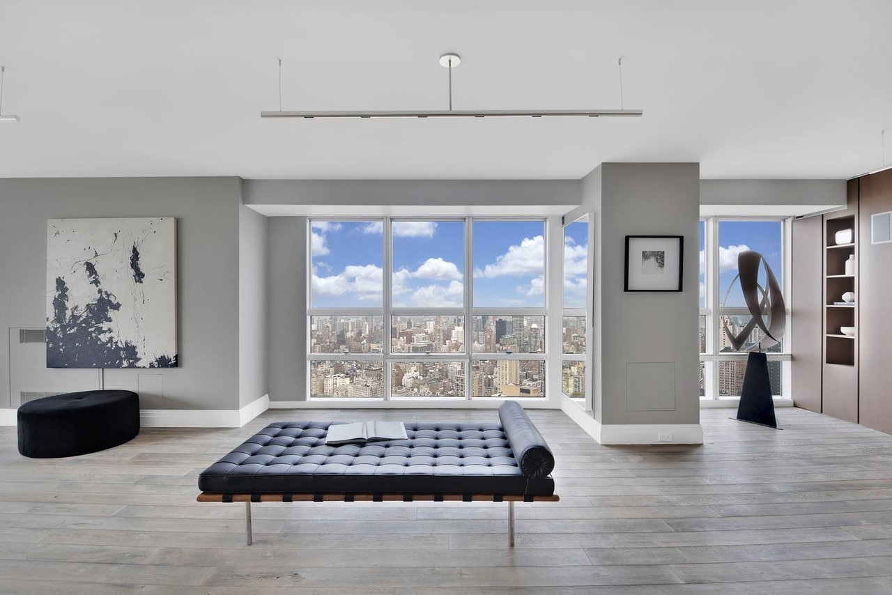 Modern living room with a black chaise lounge and floor-to-ceiling windows overlooking the city skyline.