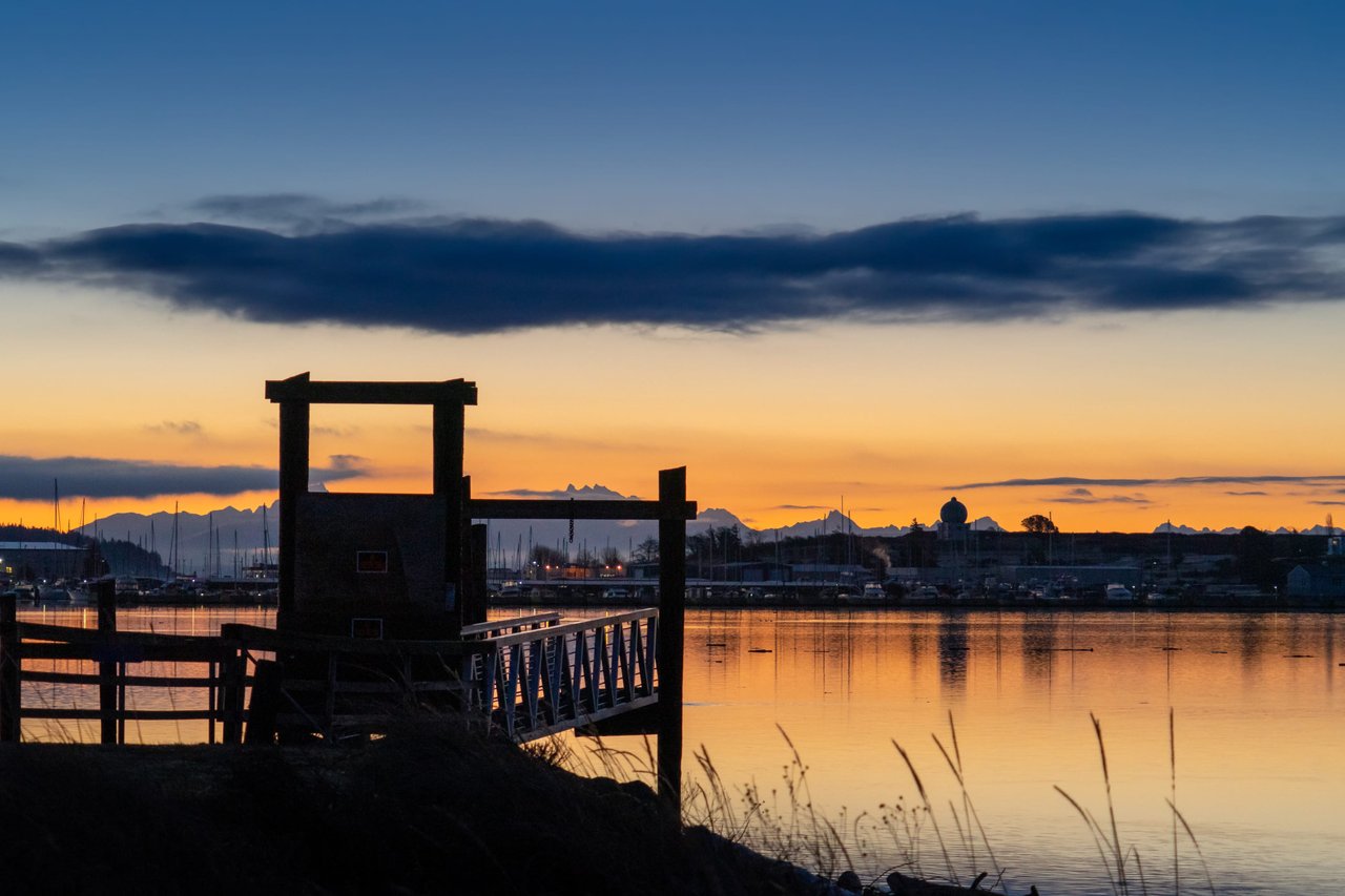 Sunset over a lake with a dock and mountains in the background. The sky is ablaze with color, and the water is calm and reflective.