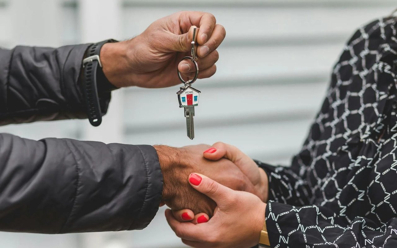 Two people shake hands as one hands over a key with a house-shaped keychain.