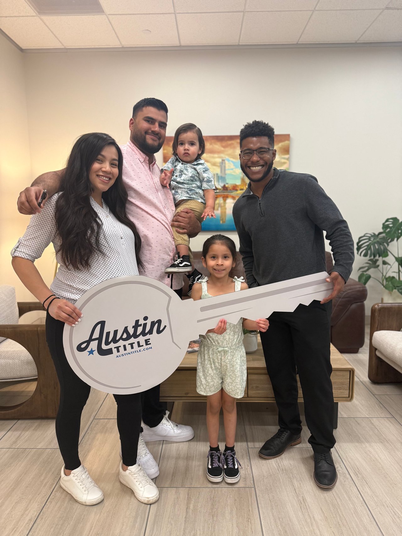 A family and real estate agent pose with an oversized Austin Title key sign.