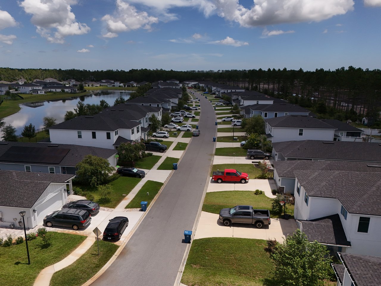 Aerial view of a residential neighborhood with a pond beside rows of homes.