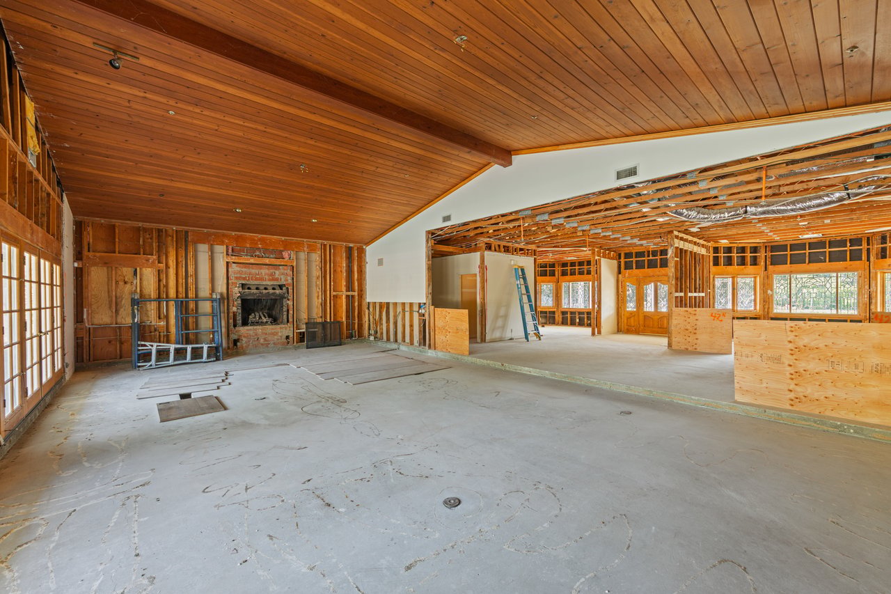 Renovated living area in progress, with a vaulted wood ceiling, exposed framing, and brick fireplace.