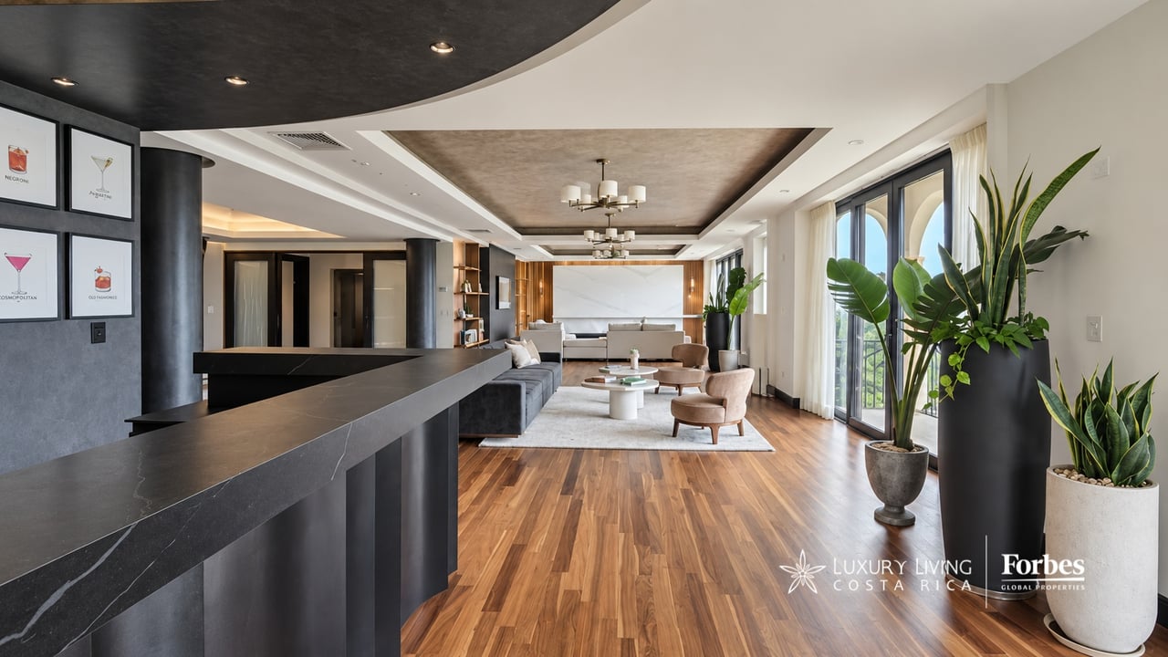 Penthouse living room with a long dark counter, wood floors, and large windows overlooking greenery.