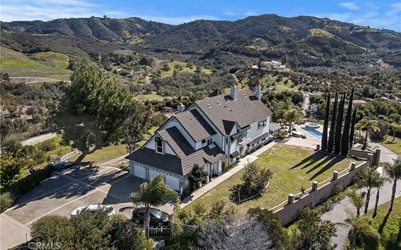 Aerial view of a large hillside home with a pool, tall cypress trees, and mountain views.