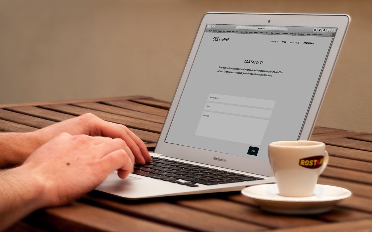 Hands typing on a laptop displaying a contact page beside an espresso cup on a wooden table.