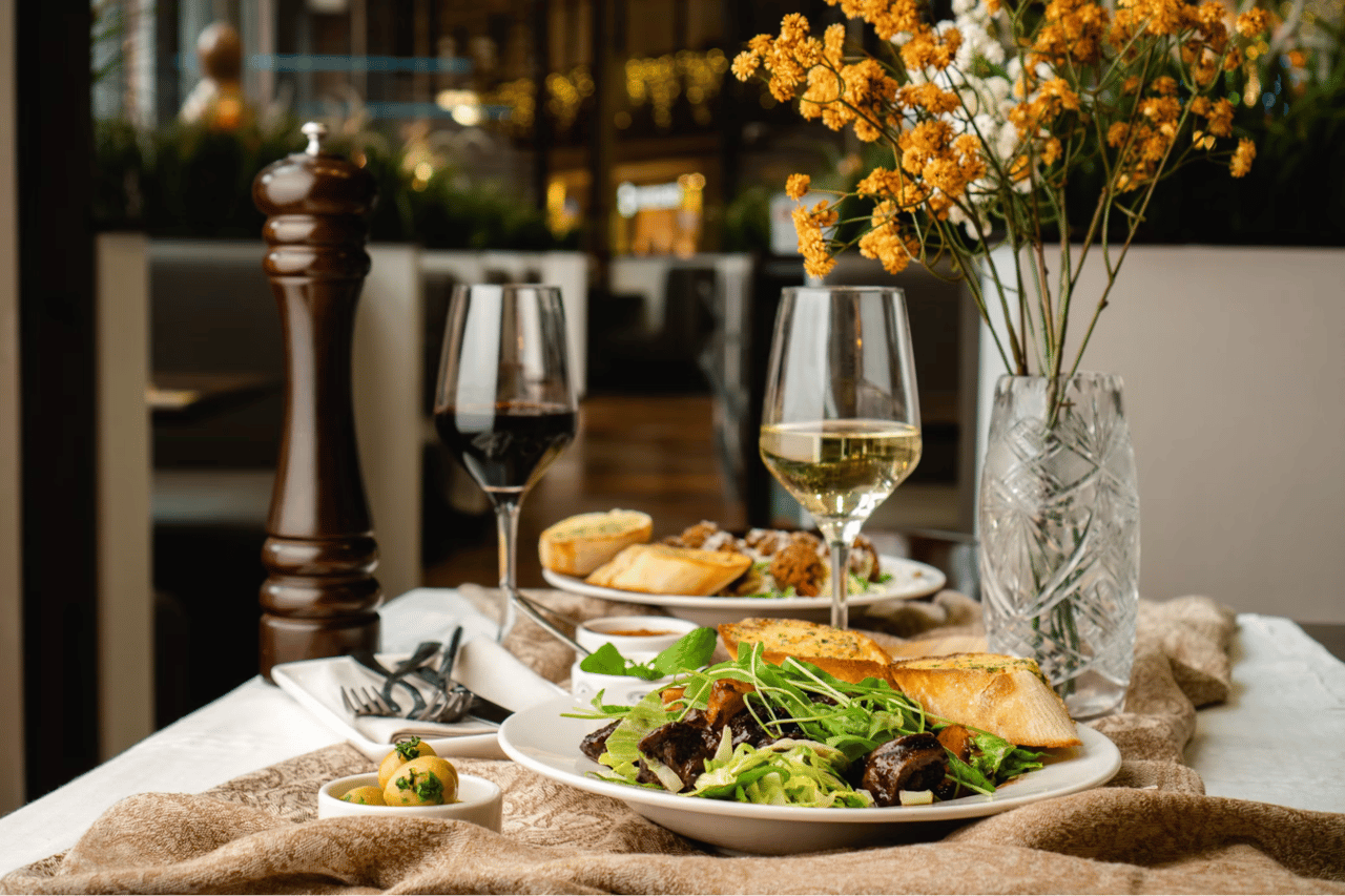 Restaurant table with plated food, wine glasses, bread, and yellow flowers.