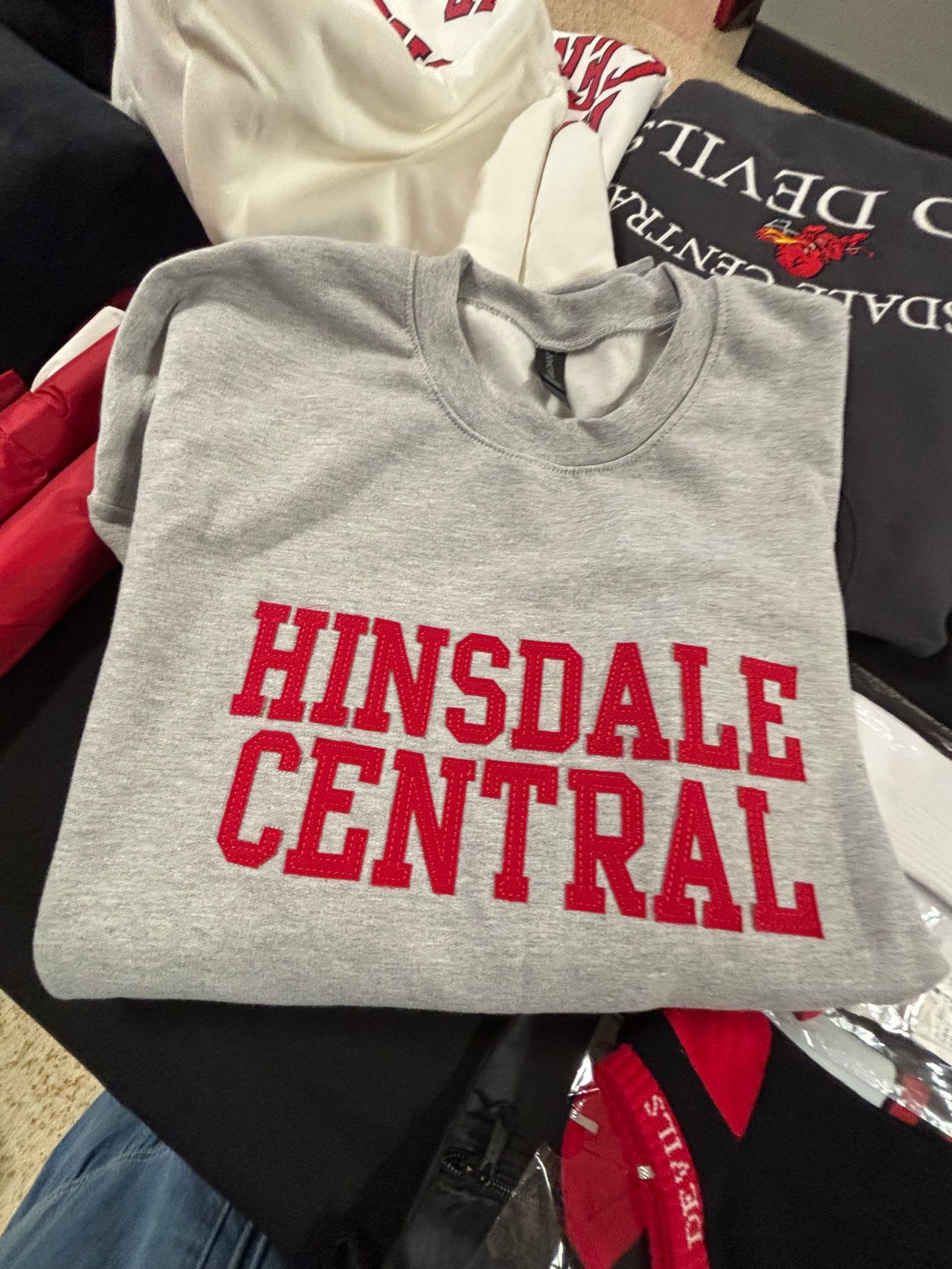 Gray Hinsdale Central sweatshirt with bold red lettering, folded over other school apparel.