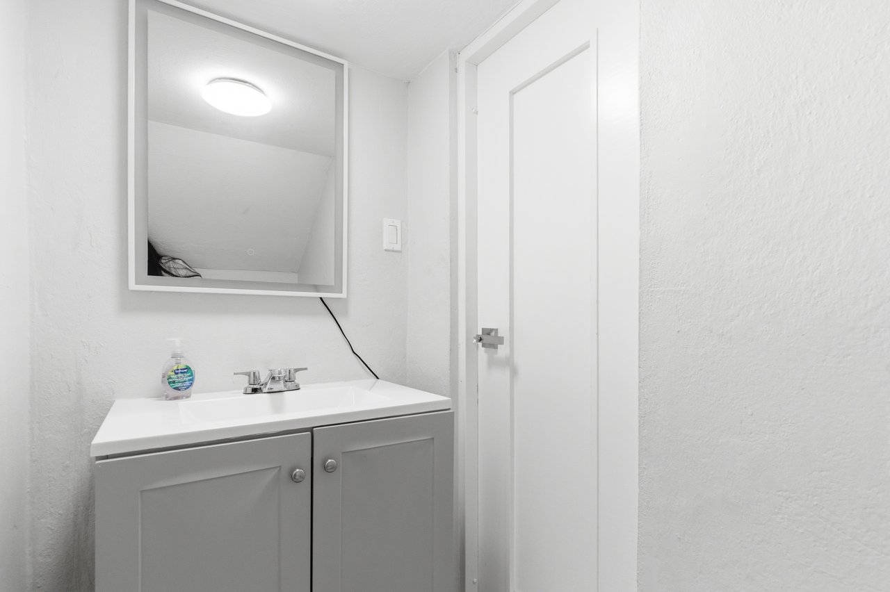 Bathroom vanity with a white sink, chrome faucet, and large wall mirror beside a closed door.