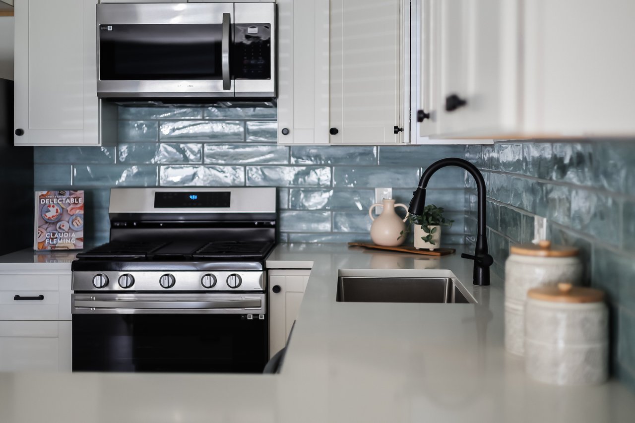 Kitchen with white cabinets, blue-gray tile backsplash, stainless-steel appliances, and a deep sink.