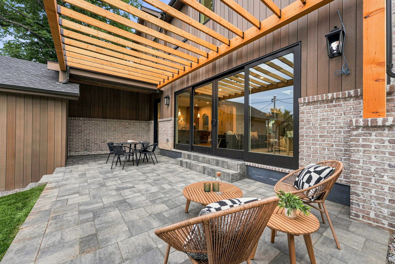 Patio with a timber pergola, gray stone pavers, and wicker seating beside sliding glass doors.