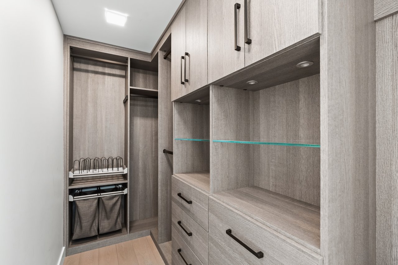 Walk-in closet with gray built-in cabinetry, glass-edged shelves, drawers, and laundry storage.