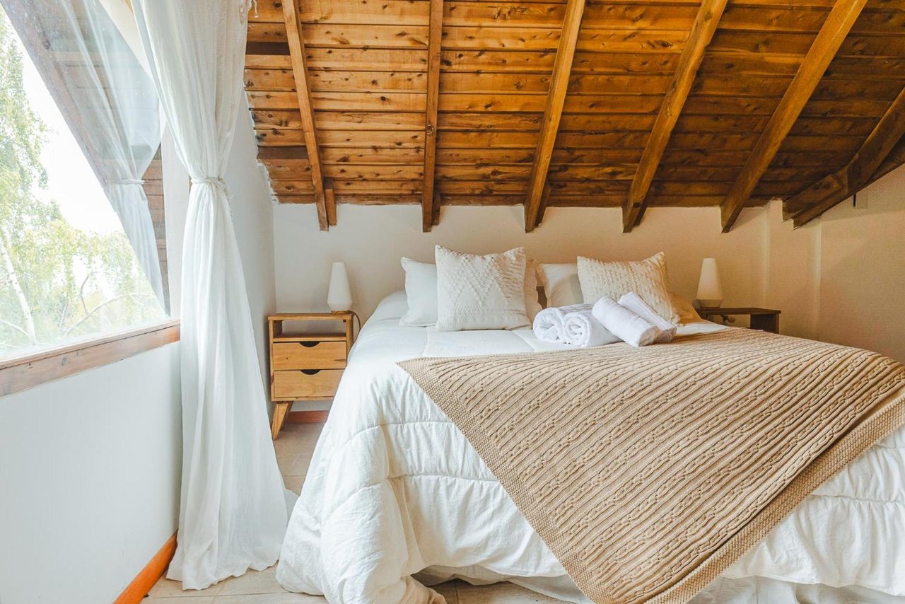 Boutique hotel bedroom with a white bed, folded towels, and exposed wooden ceiling beams.