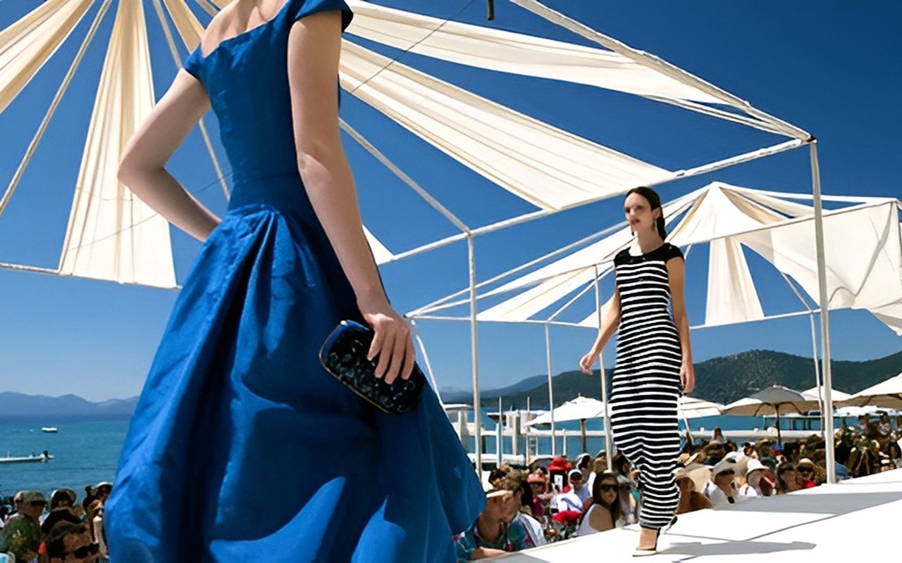 Models walk an outdoor lakeside runway beneath cream canopies, with spectators and mountains in the background.