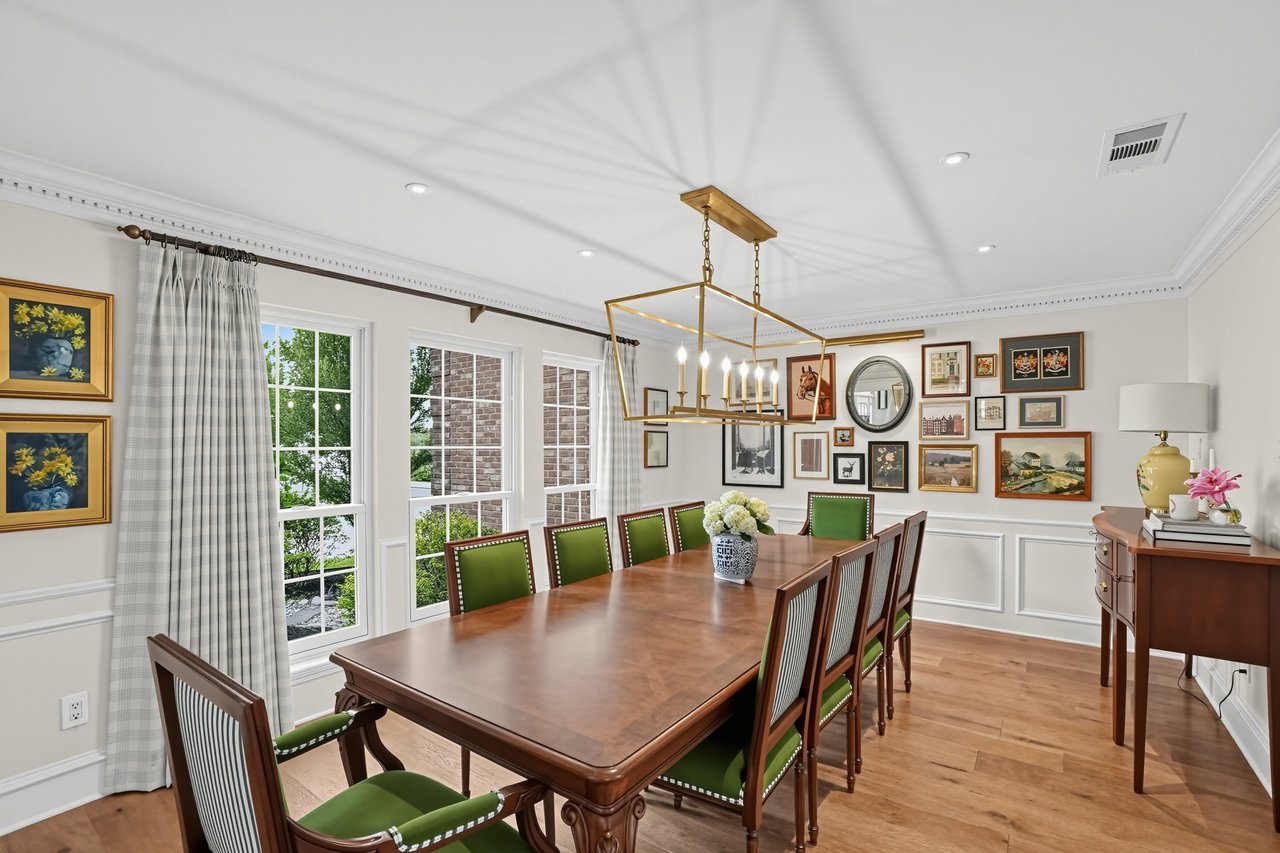 Dining room with a long wooden table, green chairs, large curtained windows, and a brass chandelier.