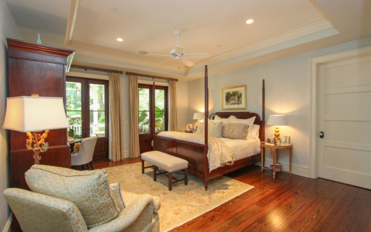 Master bedroom with a dark wood four-poster bed, hardwood floors, and French doors overlooking greenery.