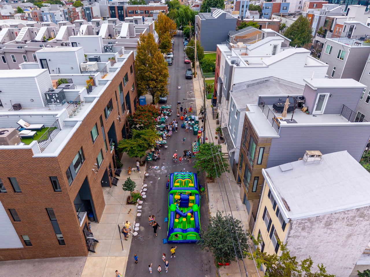 Aerial view of a neighborhood block party with tables and a colorful inflatable obstacle course.