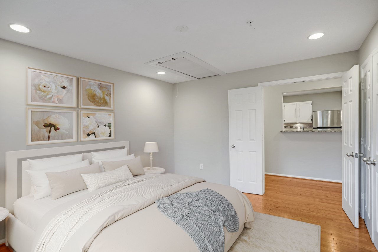 Furnished bedroom with a large white bed, floral wall art, and an open doorway to the kitchen.