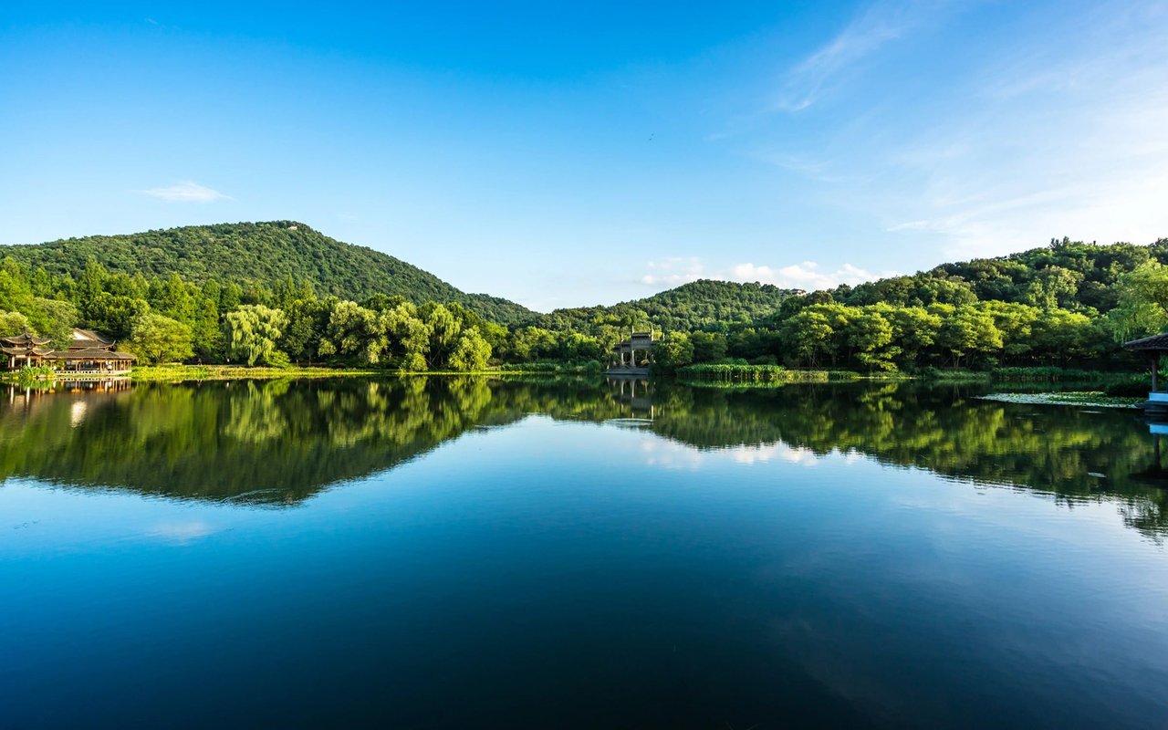 Lake reflecting forested hills and a pavilion beneath a clear blue sky.