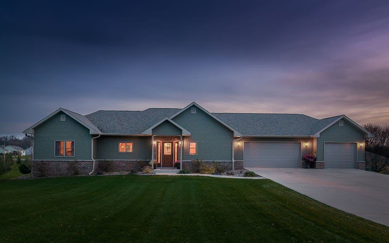 Gray-green single-story home with a covered entry and three-car garage at dusk.