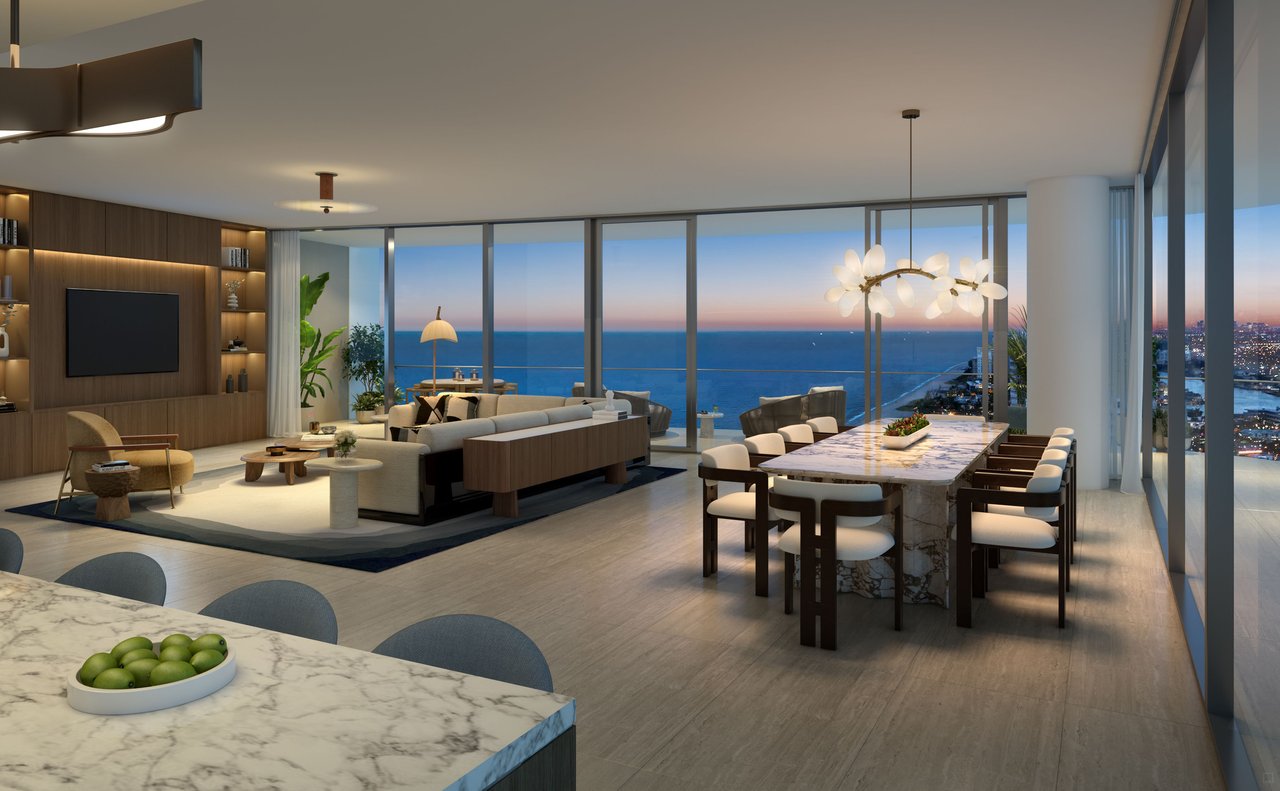 Furnished living and dining room with floor-to-ceiling windows overlooking the ocean at dusk.