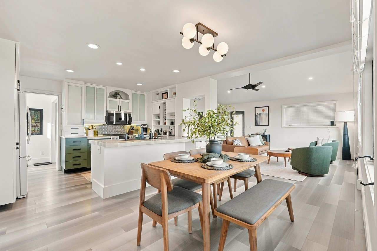 Open-plan kitchen and living area with a green island, wooden dining table, and teal lounge chairs.