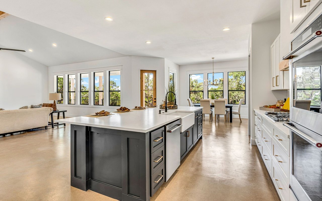 Open-plan kitchen with a large charcoal island, white cabinetry, and windows overlooking trees.