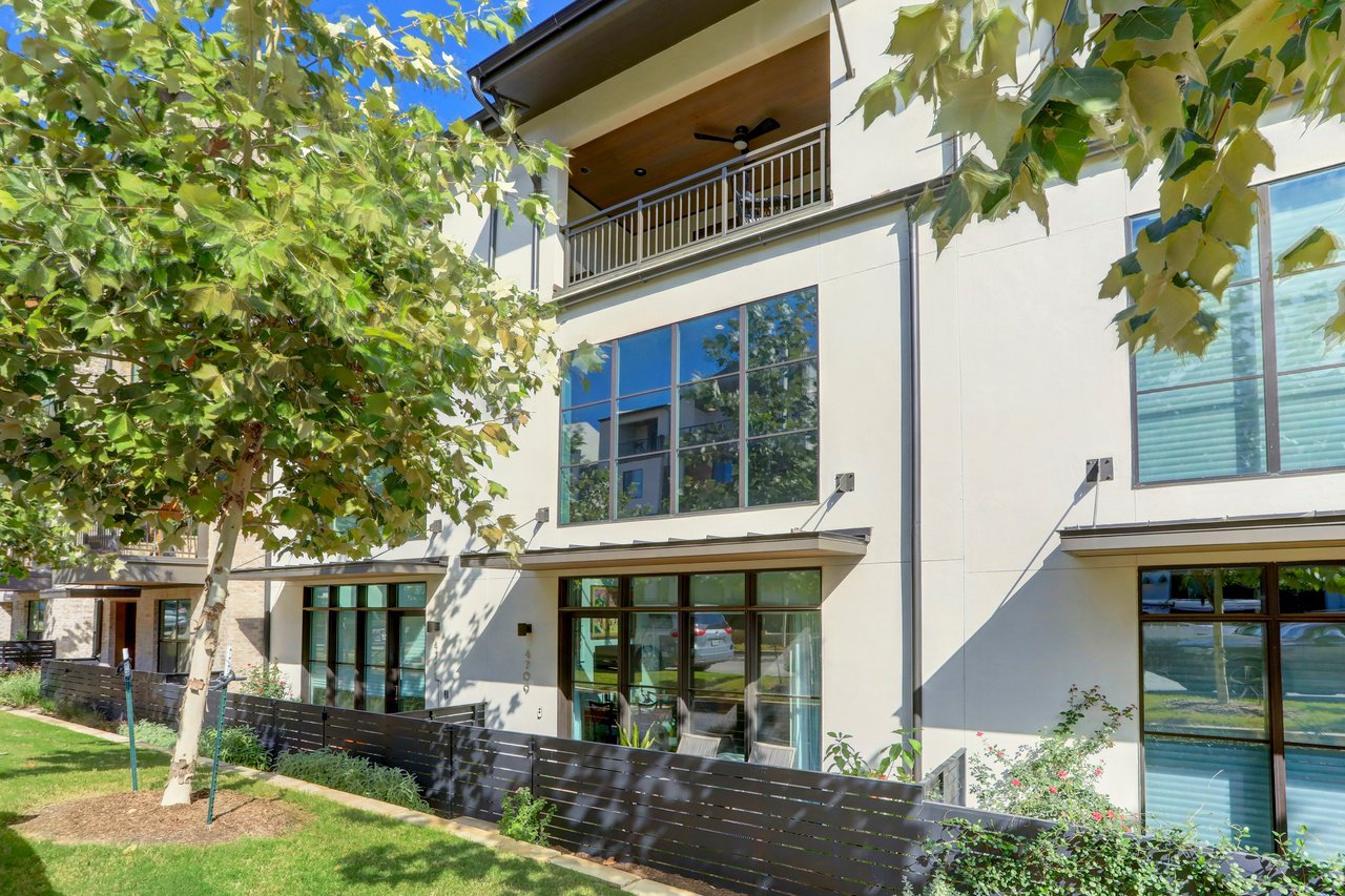 Front elevation of a three-story modern townhome at The Grove, 4709 Unity Circle #273, Austin, TX 78731 (Rosedale / Central Austin), with mature oak trees and a fenced front patio area maintained by the HOA. Built by Milestone Community.