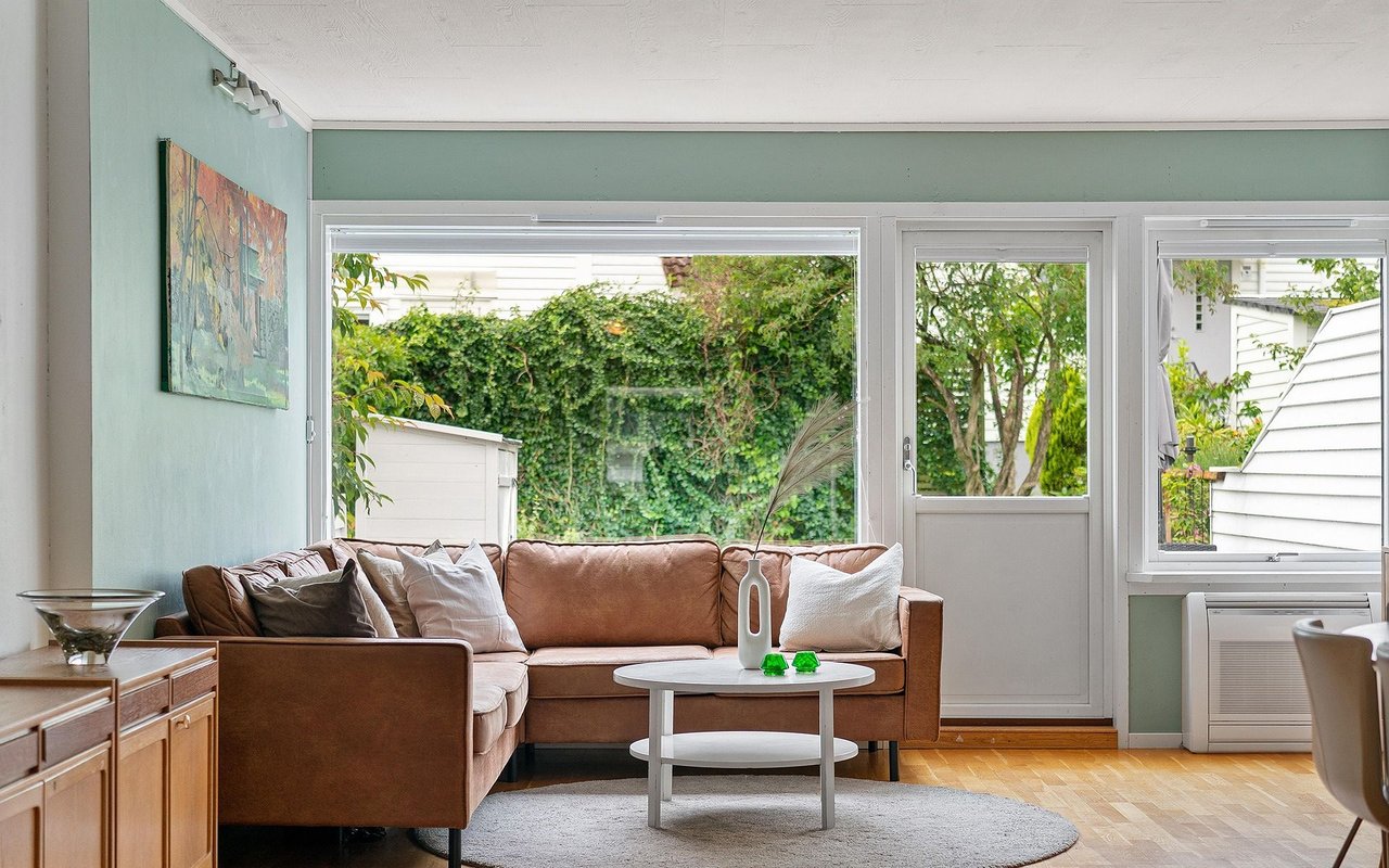 Living room with a brown leather sofa, large garden-facing windows, and green pet toys on the coffee table.