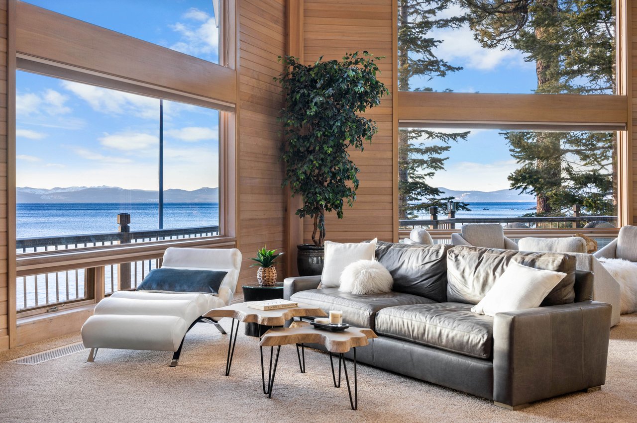 Furnished living room with expansive windows overlooking Lake Tahoe and distant mountains.