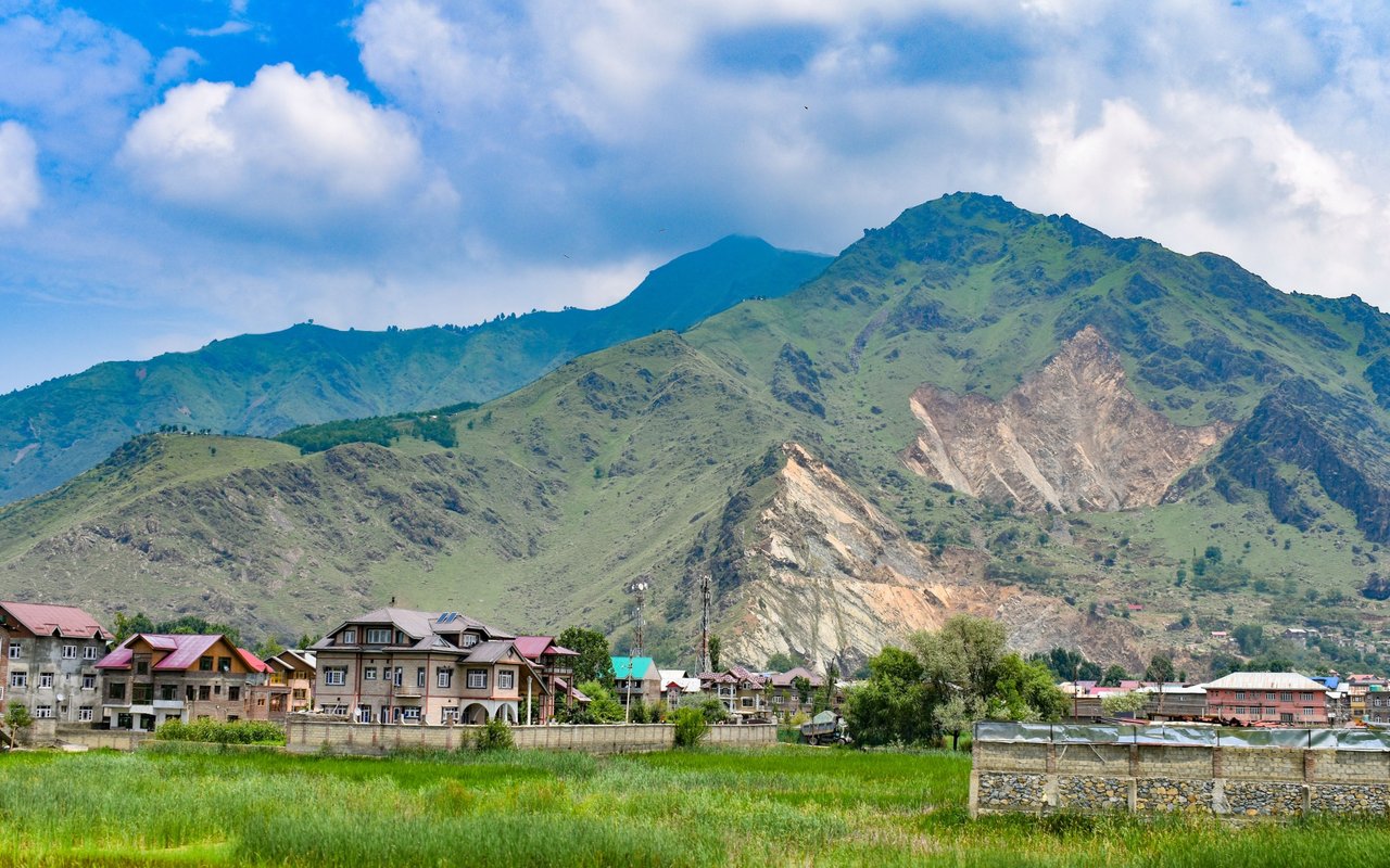 Green mountain ridges rise behind a neighborhood of homes and grassy fields.