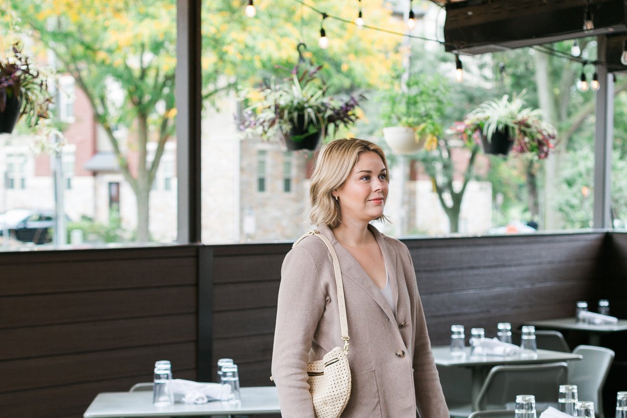 A portrait of Cait Berry of Insiders Realty walking on a covered cafe patio with hanging plants and bistro tables in Verona, WI, representing the local expertise and confidence required to strategically price a home for maximum sale value in the current Dane County market.