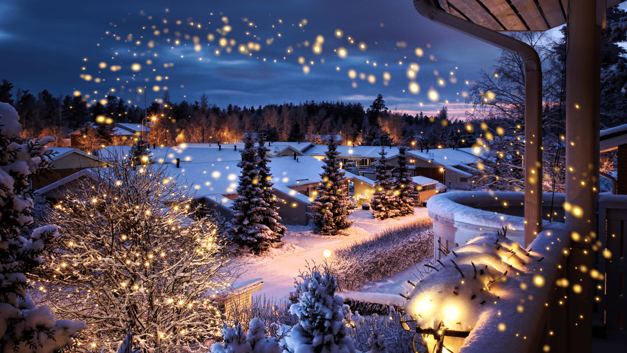 Snow-covered neighborhood at night, viewed from a porch with warm lights glowing among the trees.