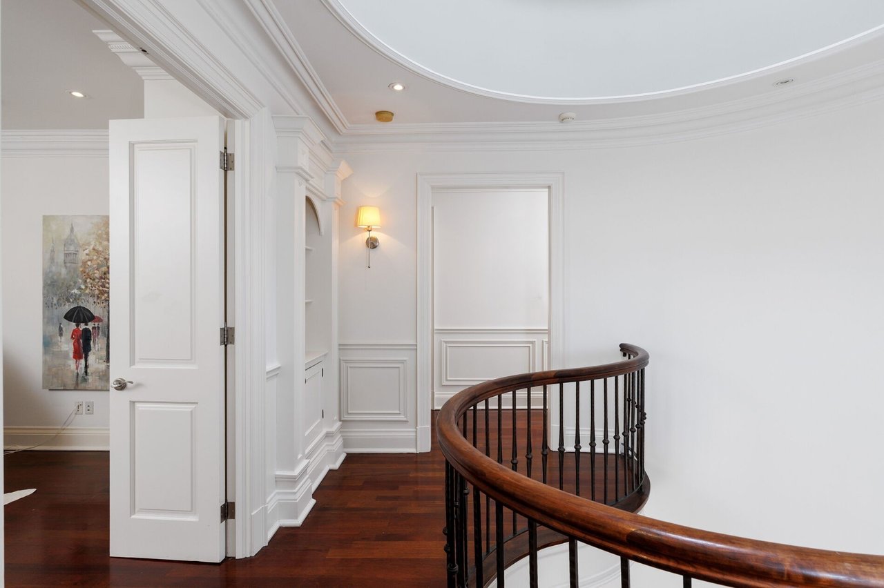 Upstairs landing with a curved dark wood railing, hardwood floors, and ornate white molding.
