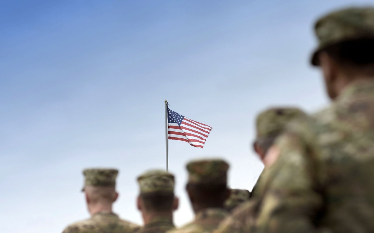 Uniformed soldiers stand beneath an American flag.