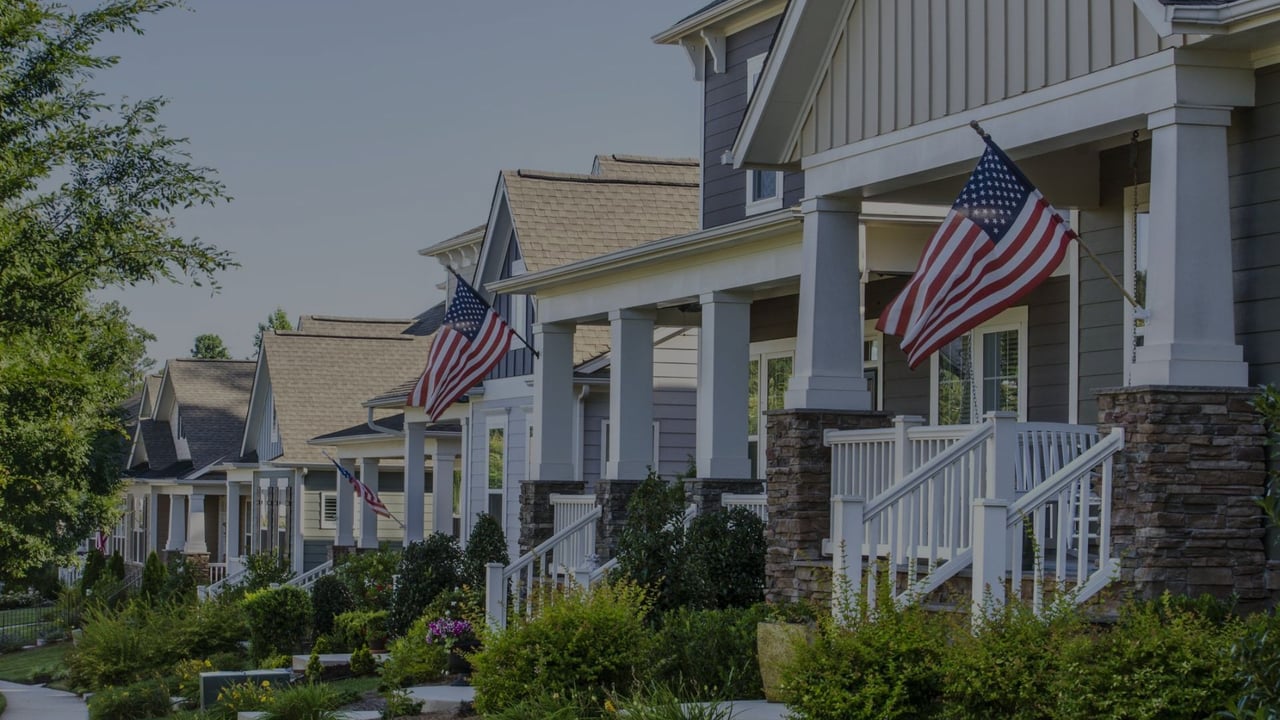 Suburban homes with covered porches, American flags, and landscaped front gardens.