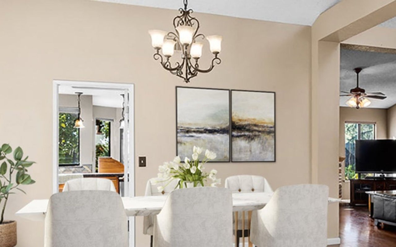 Dining room with a white table, upholstered chairs, chandelier, and adjoining living room.