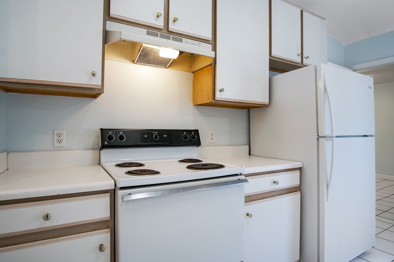 A clean kitchen with white cabinets, a black electric stove, and a white refrigerator. The lighting is warm, creating a cozy, simple atmosphere.