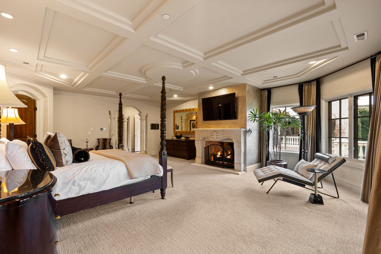 Luxury bedroom with a four-poster bed, fireplace, and tall curtained windows.