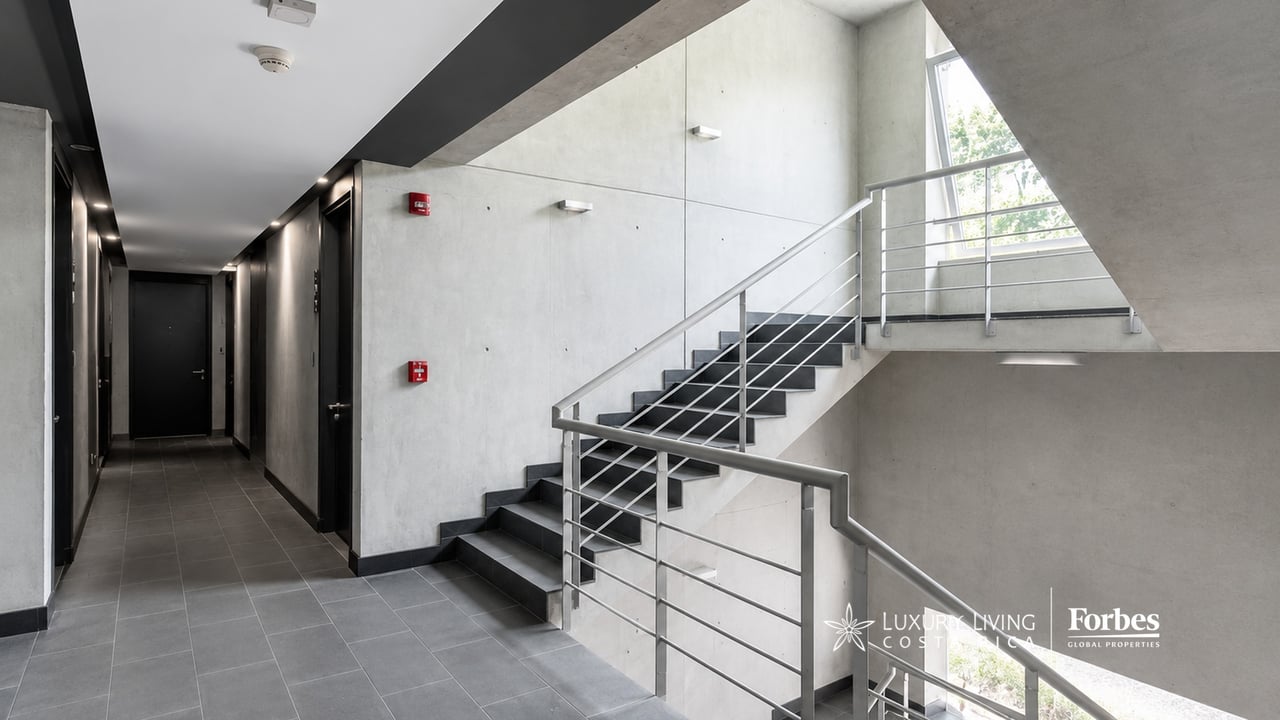 Modern apartment stairwell with gray tile, concrete walls, metal railings, and tall windows.