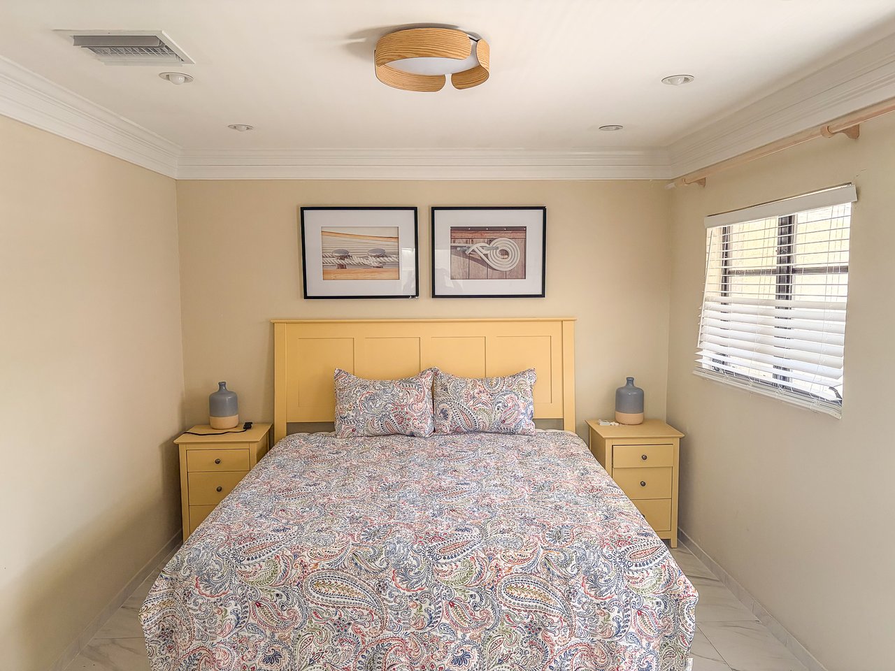 Furnished bedroom with a paisley-covered bed, mustard-yellow headboard, and matching bedside tables.