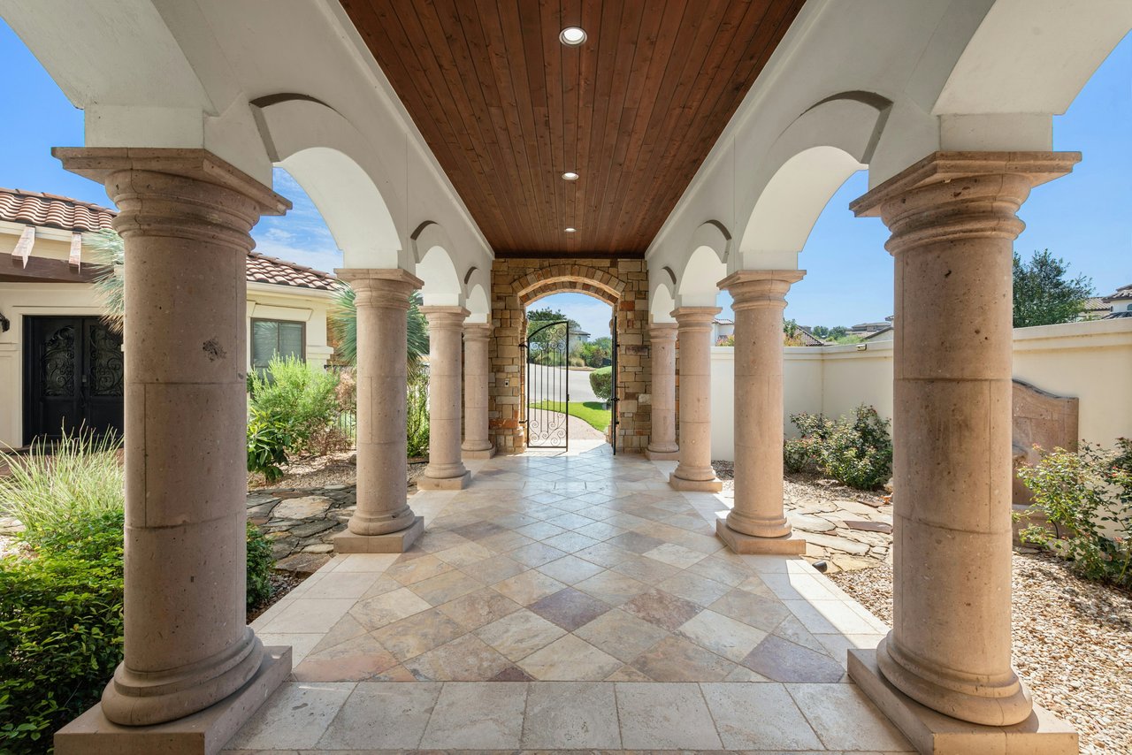 Covered entry walkway with stone columns, white arches, a wood ceiling, and a wrought-iron gate.