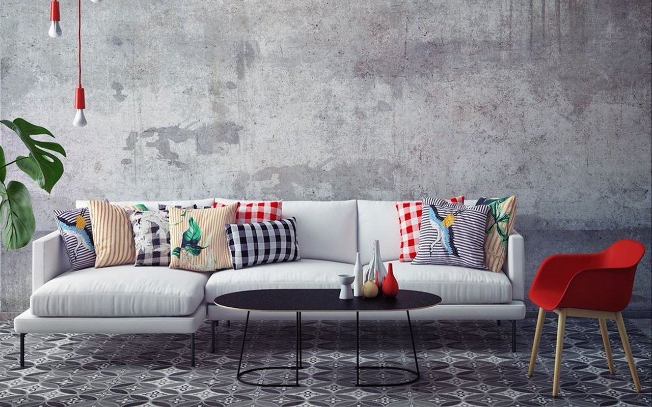 Living room with a white sectional, colorful pillows, red chair, and concrete wall.