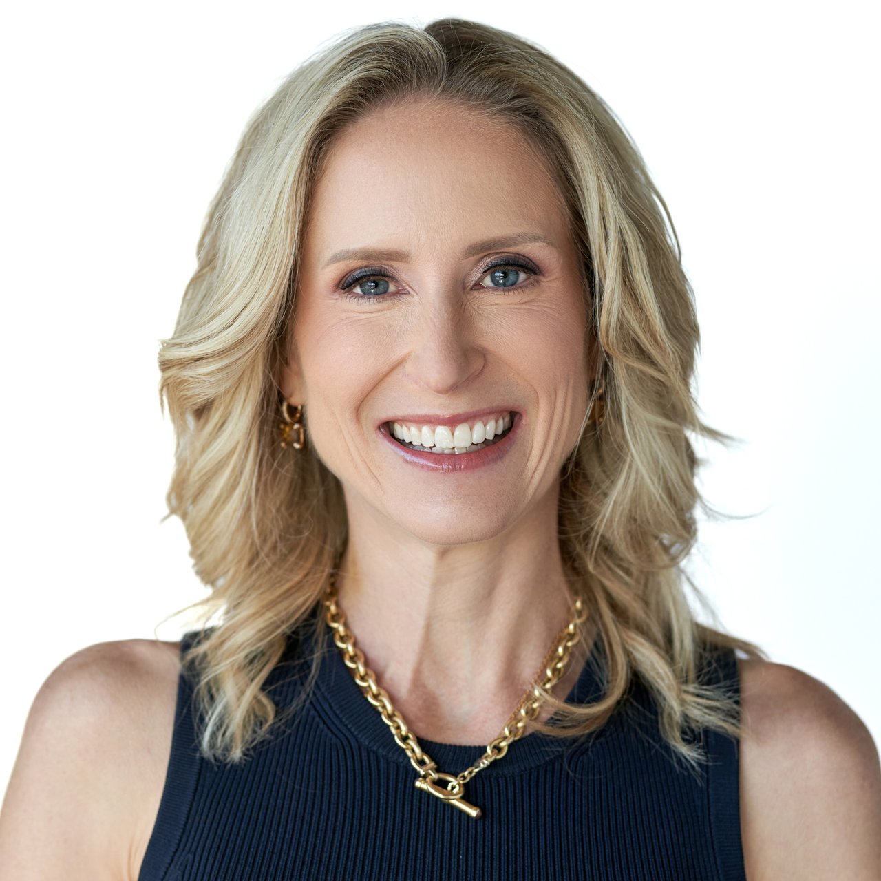 Lizzy Conroy smiling in a navy top and gold jewelry.