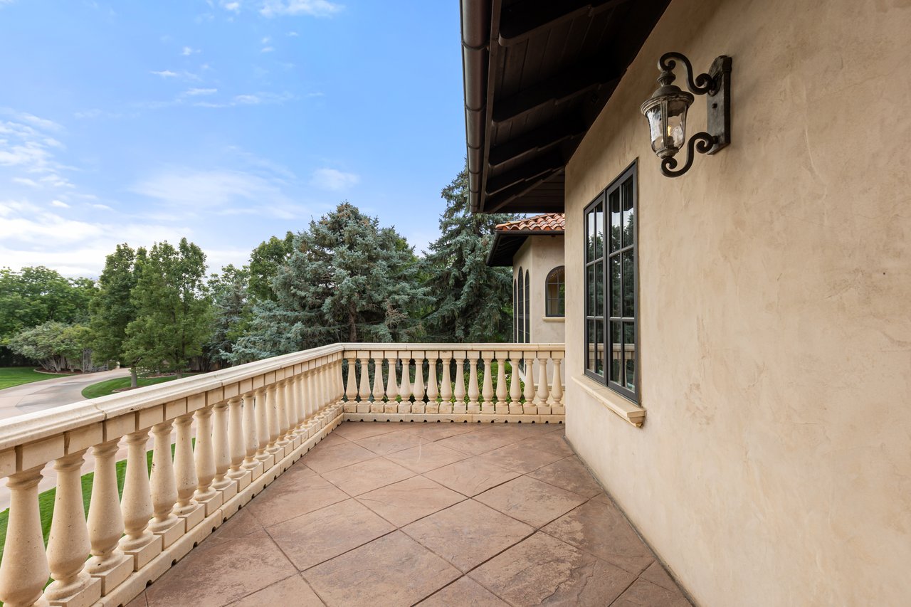 Tiled balcony with a cream balustrade, stucco wall, and views of mature trees.