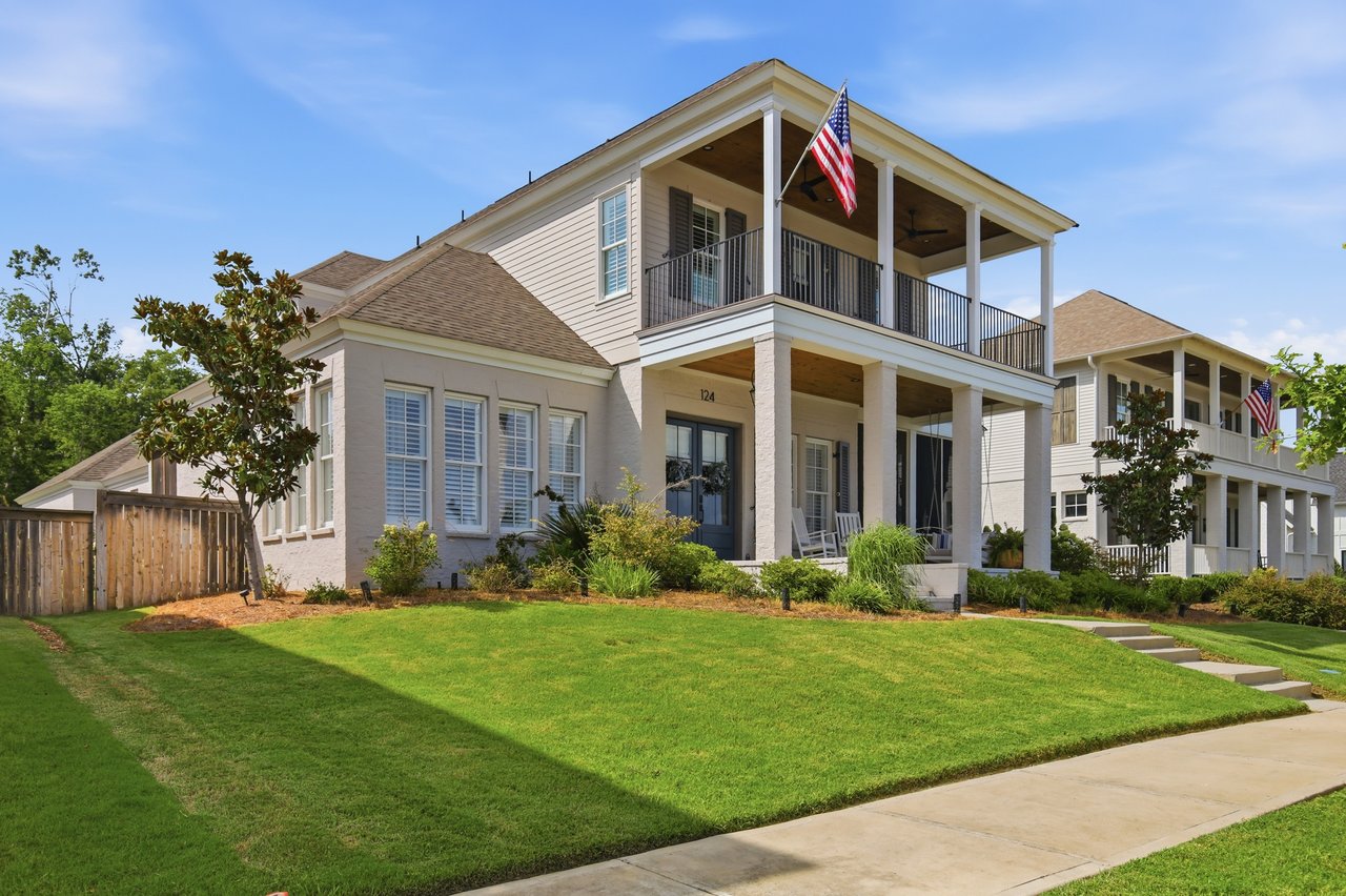Two-story home with a covered balcony, American flag, and broad front lawn.
